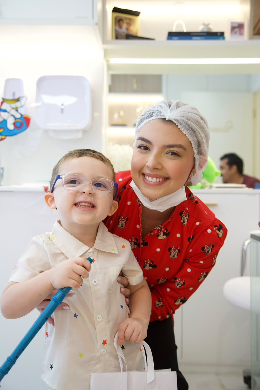 Dra. Thirza Nunes sorrindo abraçada a um menino no consultório infantil